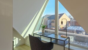 Una habitación moderna con techo inclinado, una mesa de vidrio, una silla y una planta en maceta.