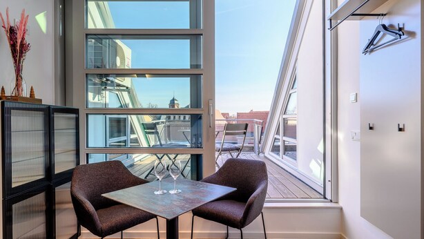Una habitación moderna con un ventanal grande, una mesa con dos sillas y un jarrón decorativo.