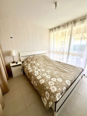 Ein Schlafzimmer mit Bett, Nachttisch, Lampe und Vorhängen.