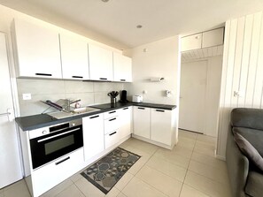 A modern kitchen with white cabinets, a black countertop, and a built-in oven. - Appartement Coquillage by Agence Bru - 692804 (Lacanau)
