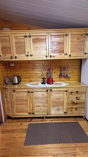 A wooden kitchen with cabinets, a countertop, a kettle, a blender, and utensils hanging on the wall. - Rustic and welcoming wooden house (Foz do Iguaçu)