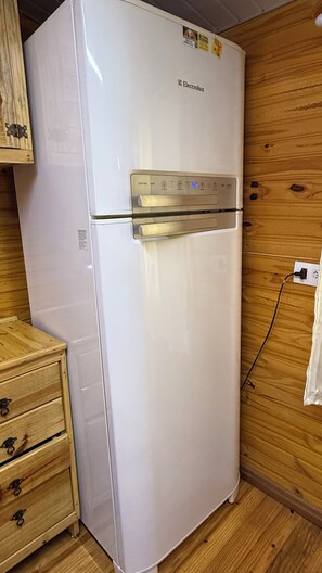 A white Electrolux refrigerator in a wooden-paneled kitchen with a wooden cabinet and a power outlet on the wall. - Rustic and welcoming wooden house (Foz do Iguaçu)