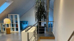 A modern loft-style living space with a mezzanine level, a staircase with metal railings, and a large potted plant. - WeinZeit4 - Premium time out at the Frank Meyer winery (Gleiszellen-Gleishorbach)