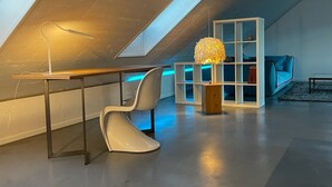 A modern loft with a sloped ceiling, a desk with a lamp, a white chair, a decorative spherical light fixture, and a blue chair. - WeinZeit4 - Premium time out at the Frank Meyer winery (Gleiszellen-Gleishorbach)