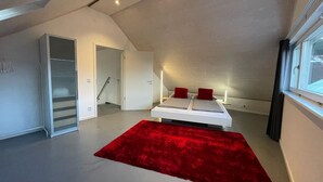 A modern bedroom with a sloped ceiling, a bed with red pillows, a red rug, and a window with a view. - WeinZeit4 - Premium time out at the Frank Meyer winery (Gleiszellen-Gleishorbach)