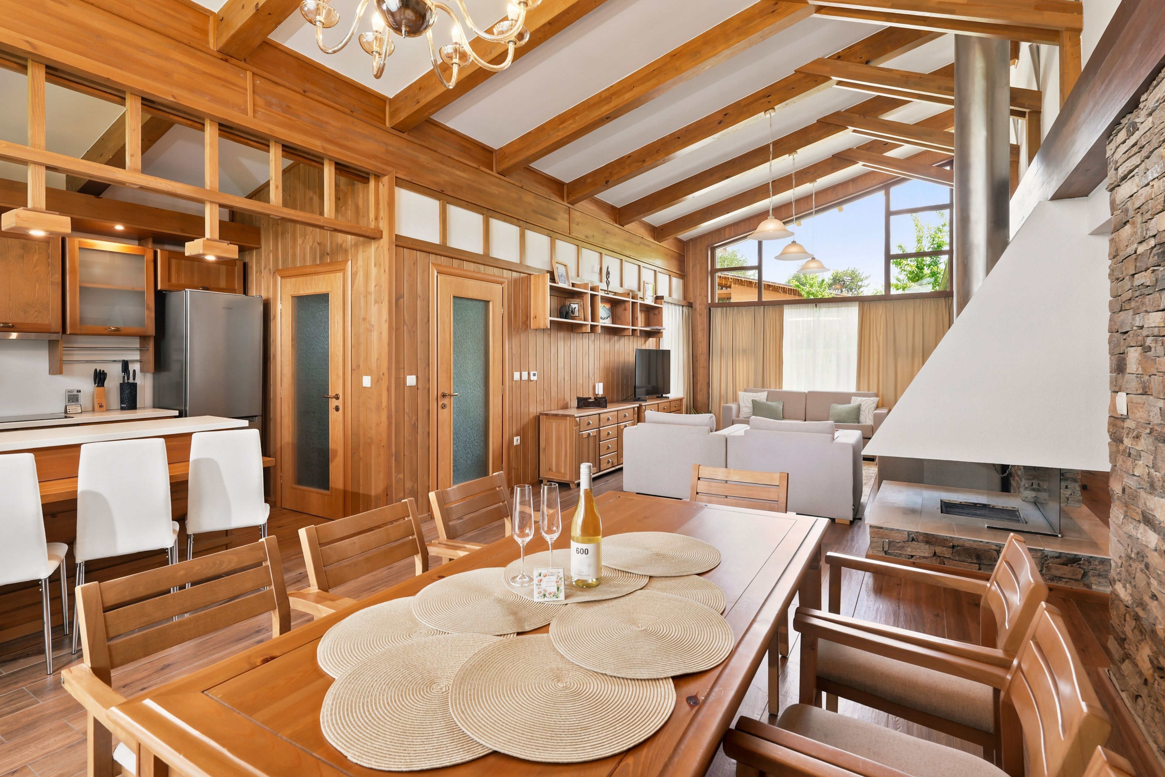 A modern kitchen with wooden cabinetry, a dining area with a table set for two, and a stone fireplace.