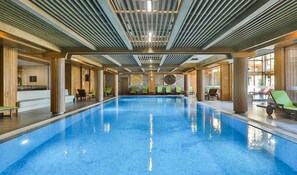Una piscina interna con acqua cristallina, colonne in legno e sedie a sdraio.