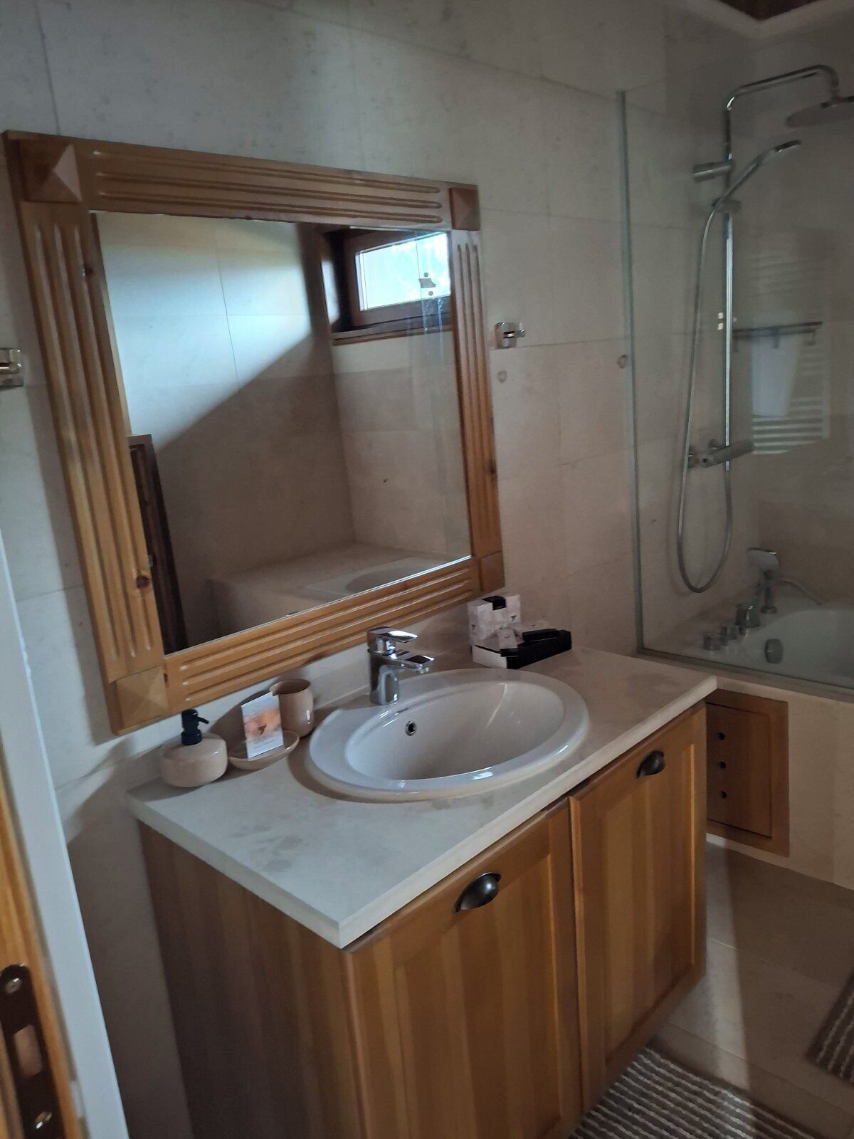 A bathroom with a wooden vanity, a large mirror, a sink, and a glass shower enclosure.