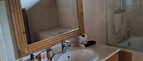 A bathroom with a wooden vanity, a large mirror, a sink, and a glass shower enclosure.