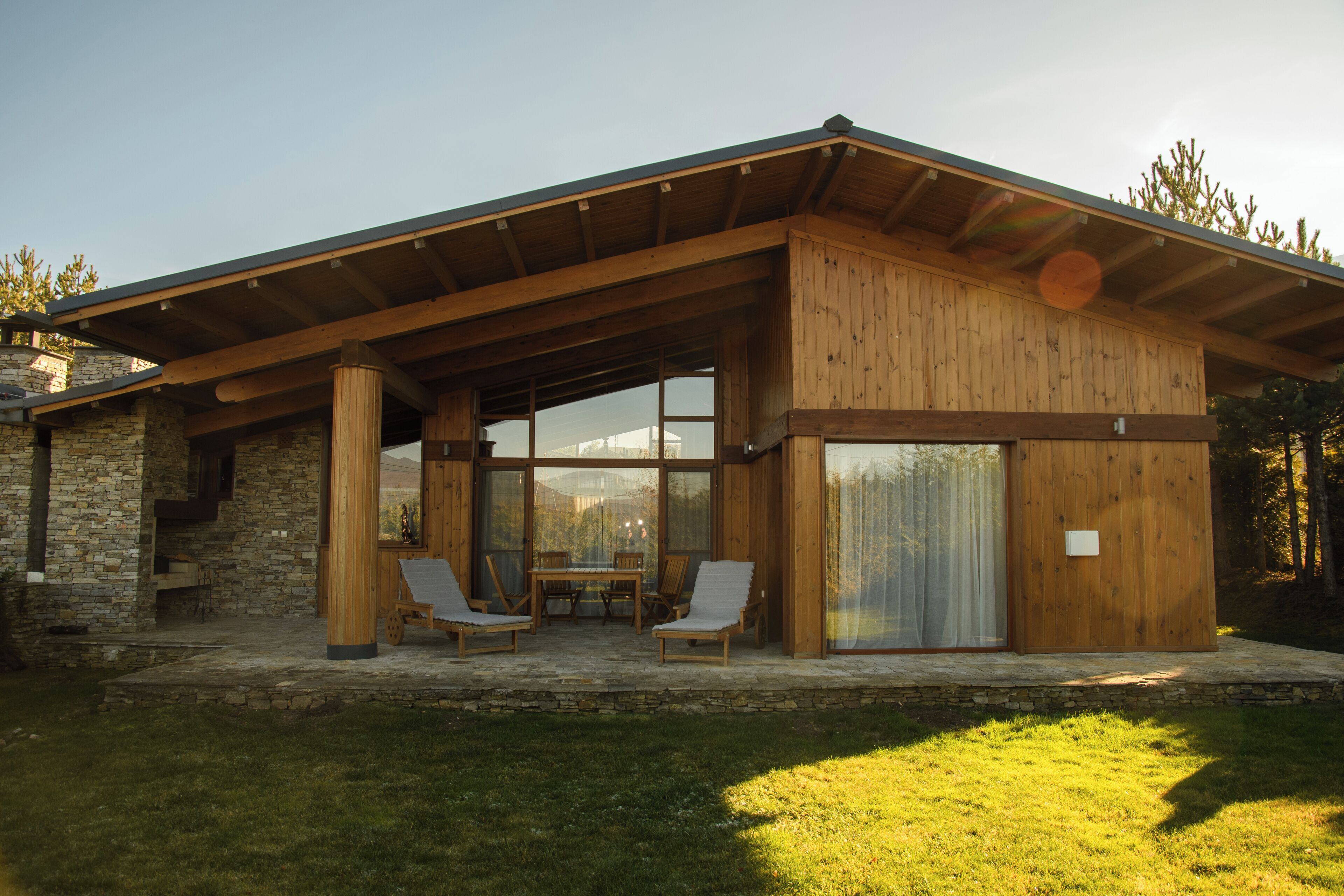 A modern house with a large patio area, stone walls, and a wooden deck.