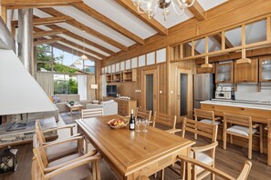 A spacious kitchen with wooden cabinetry, a dining area with a wooden table and chairs, and a large window providing natural light. - Pirin Golf Villas (Razlog)