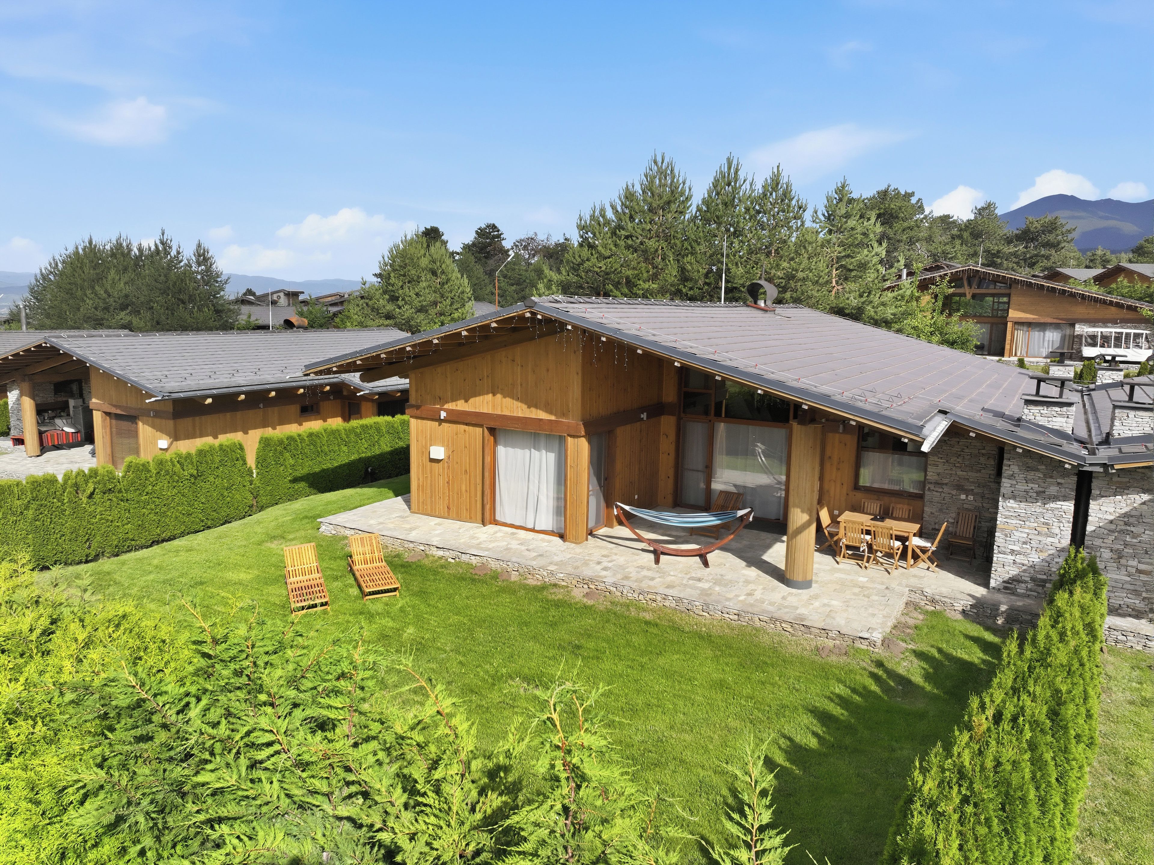 A wooden cabin with a patio, a hammock, and a stone wall.