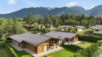 A cluster of wooden cabins with sloped roofs, surrounded by lush greenery and mountains in the background.