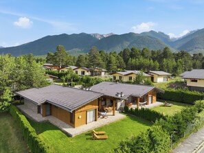 A cluster of wooden cabins with sloped roofs, surrounded by lush greenery and mountains in the background.