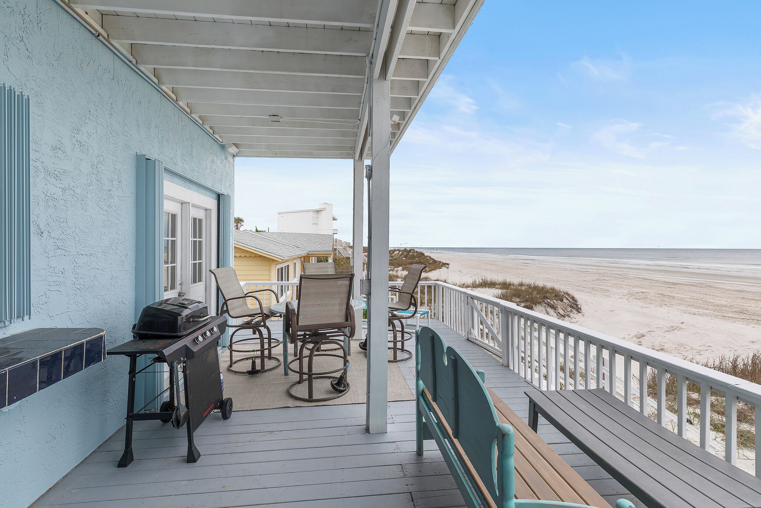 Une terrasse couverte équipée d’un barbecue, de chaises et offrant une vue sur la plage.