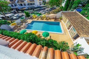 Una piscina en la azotea con varios sillones de tomar el sol y sombrillas, rodeada de tejas de arcilla y vegetación.