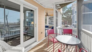 Une terrasse extérieure couverte, dotée d’une porte vitrée donnant sur un espace patio aménagé avec des fauteuils et une table en osier.
