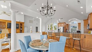 Une cuisine spacieuse avec des meubles en bois, un îlot central et un coin repas agrémenté de chaises bleues et d’une table ronde.