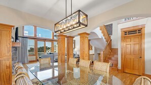 Ein geräumiges Wohnzimmer mit einem Esstisch aus Glas, Korbstühlen, einer Holztreppe und einem großen Fenster.
