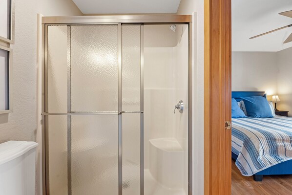 A room with a glass shower door, a bed with a blue and white striped bedspread, and a nightstand with a lamp. - Eventide: Views of the Golf Course | Private Pool | Ensuite Bedrooms (Corolla)