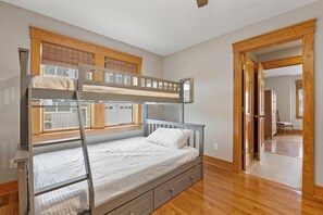 Een stapelbed met een ladder, een enkel bed beneden en een houten vloer.
