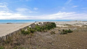 Una spiaggia con una recinzione in legno e vegetazione rada sullo sfondo.