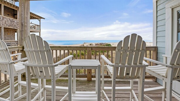 Un pontile in legno con poltrone Adirondack bianche e vista sulla spiaggia.
