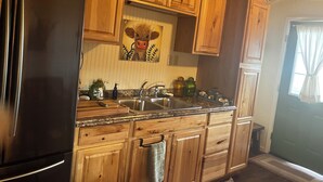 A kitchen with wooden cabinets, a stainless steel refrigerator, a sink, and a decorative cow painting.