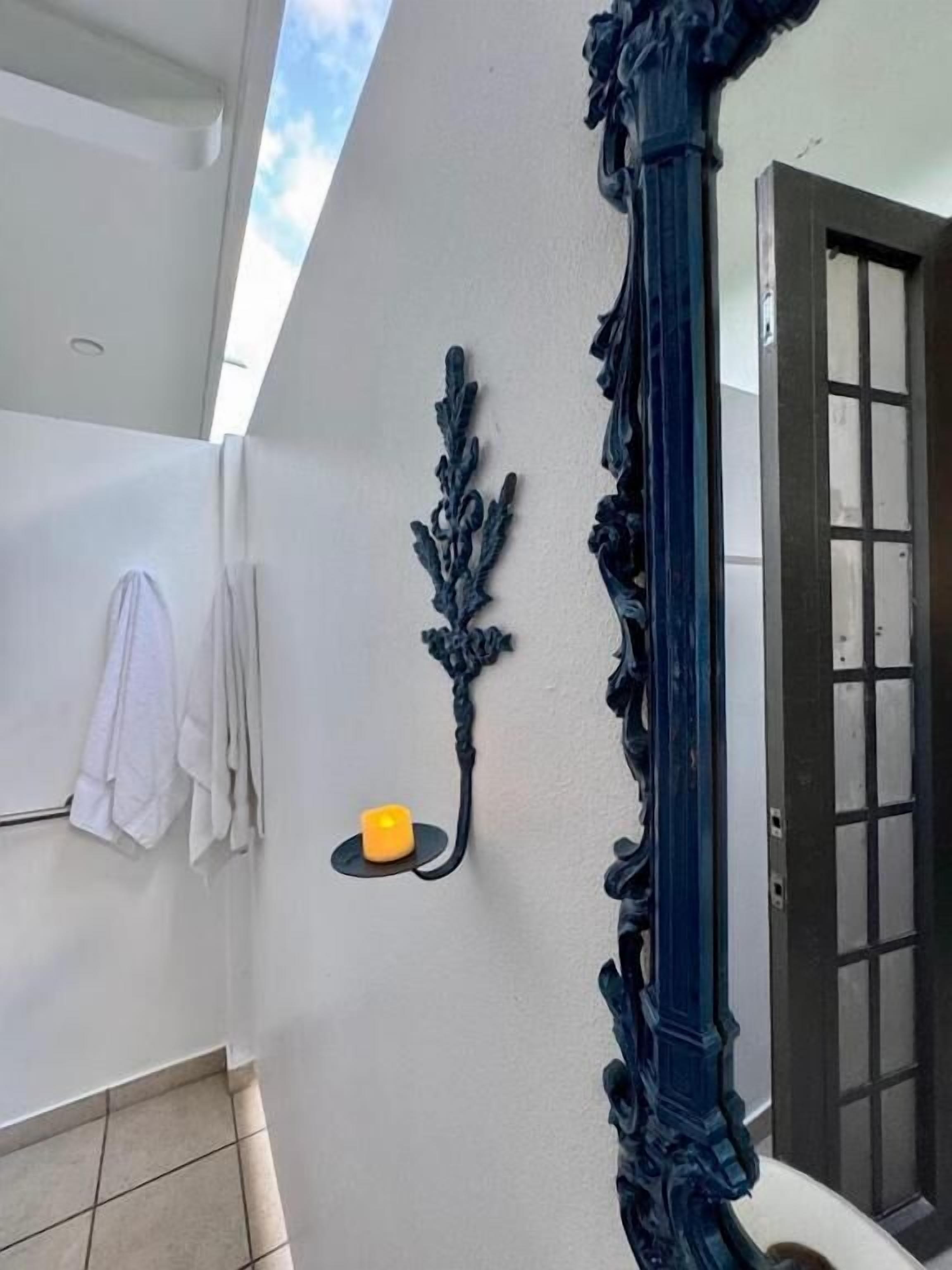 Un baño con pared blanca, un pilar decorativo azul, un estante pequeño con una vela y una puerta con paneles de vidrio.