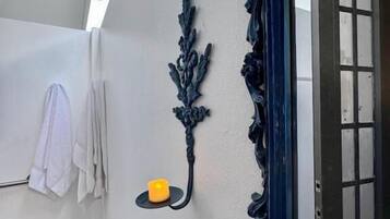 Un baño con pared blanca, un pilar decorativo azul, un estante pequeño con una vela y una puerta con paneles de vidrio.