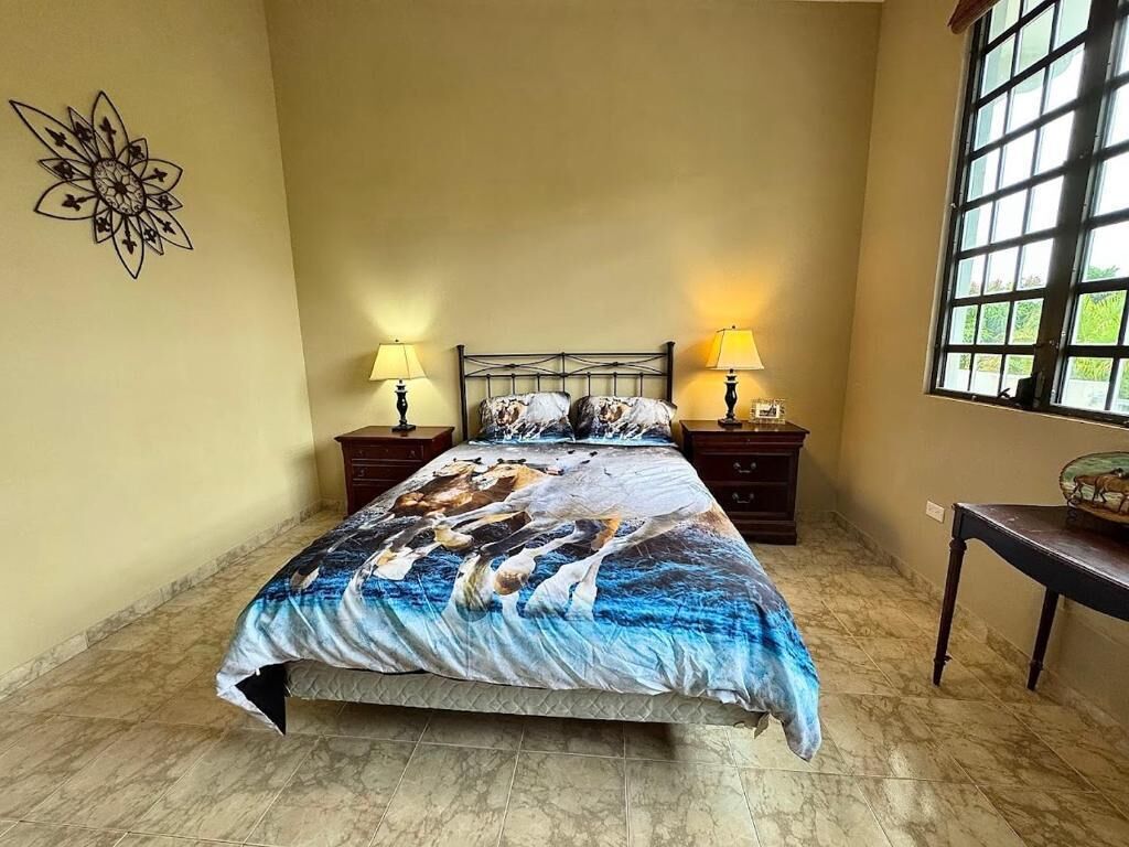 A bedroom with a bed, two bedside tables with lamps, a decorative wall piece, and a window.