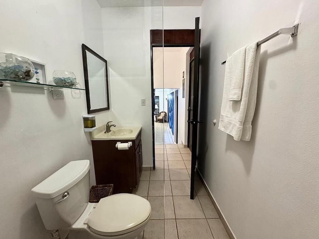 Baño pequeño con inodoro, lavabo y espejo. Una toalla cuelga en la pared.