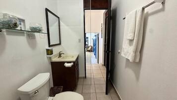 Baño pequeño con inodoro, lavabo y espejo. Una toalla cuelga en la pared.