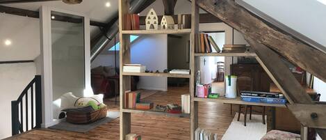 Une chambre à coucher de style « loft », avec des poutres apparentes, un plafond en pente et une bibliothèque intégrée remplie de livres et d’objets décoratifs.