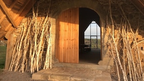 Una porta ad arco in legno che dà su una stanza con una parete in pietra e vista su alberi.