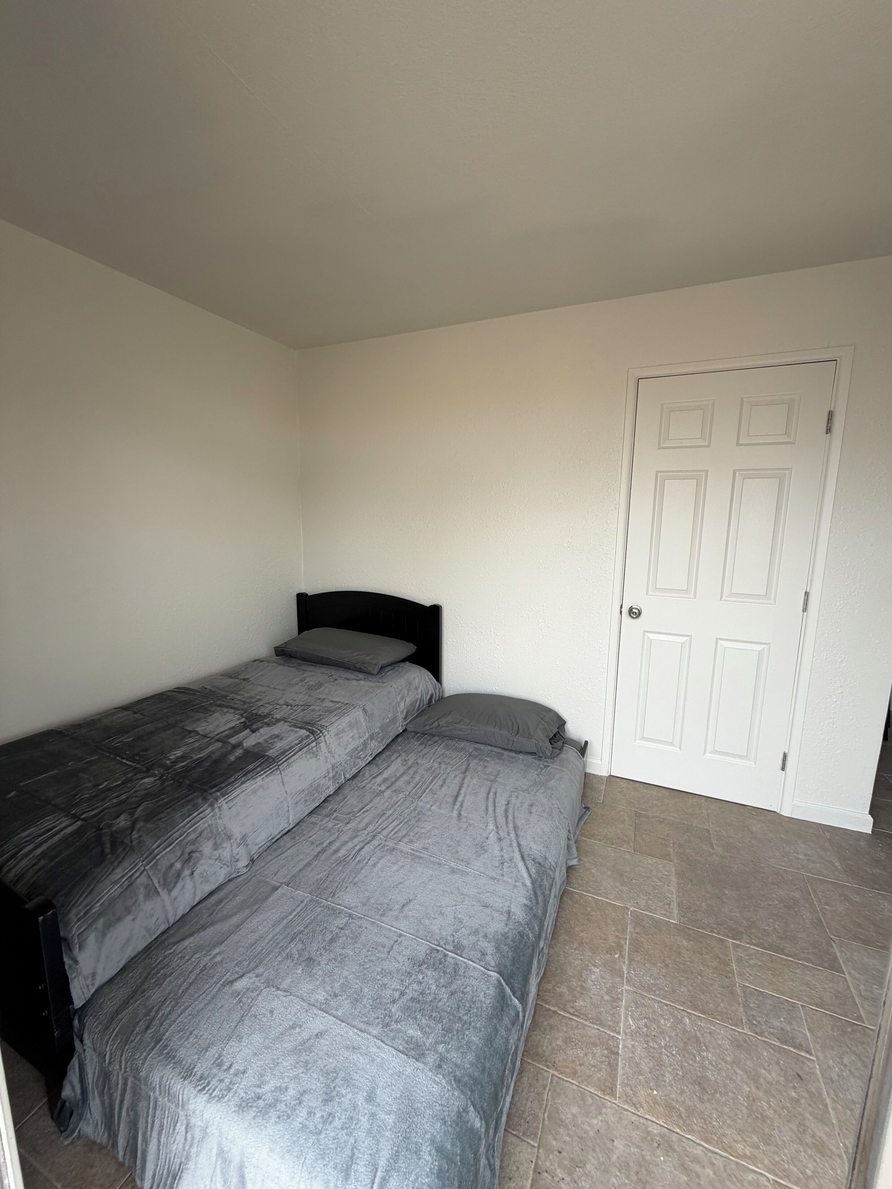 Ein Schlafzimmer mit Bett, einer Tür und Fliesenboden.