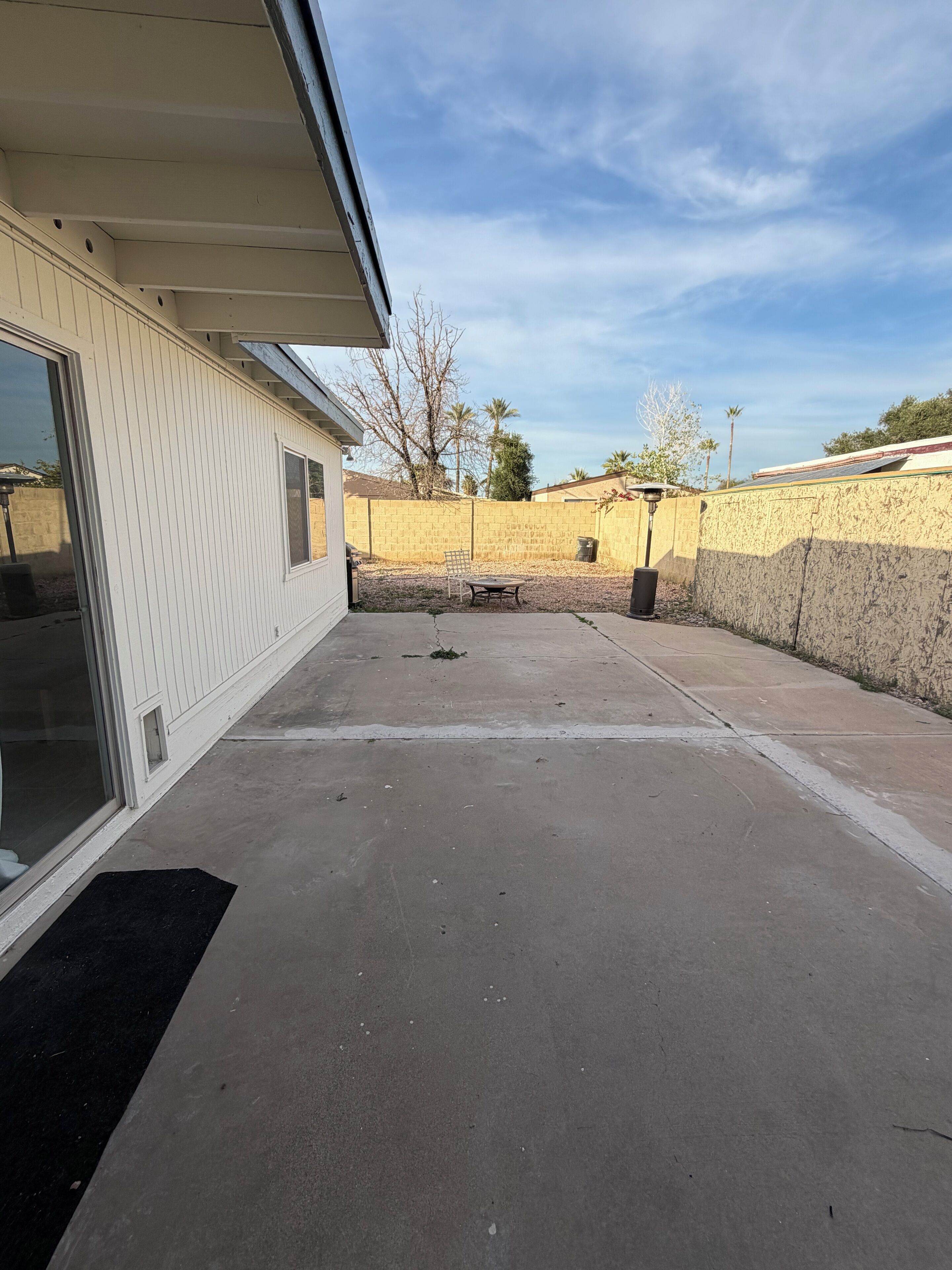 A covered patio area with a concrete floor, a metal chair, and a trash can.