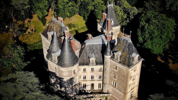Een kasteel met meerdere torens en een centraal gebouw, omringd door dichte bomen.