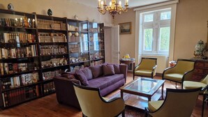 Een gezellige woonkamer met een paarse bank, houten vloer en een grote boekenkast vol boeken en decoratieve voorwerpen.