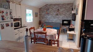 A compact kitchen with white cabinets, a dining table with chairs, a stone wall, and a TV in the living area. - Small house located in a village 15min from Langeais (Hommes)