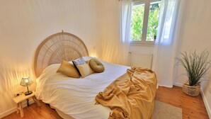 Ein ordentlich bezogenes Bett mit Kopfteil, einer Nachttischlampe und einem Fenster mit Vorhängen.