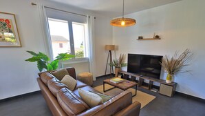 Ein modernes Wohnzimmer mit einer Ledersofa, einem Flachbildfernseher, einer Stehlampe und einem großen Fenster mit Vorhängen.
