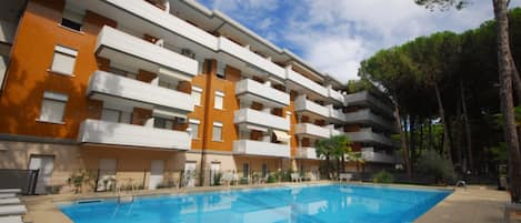 A multi-story residential building with balconies, a swimming pool, and a landscaped garden area.