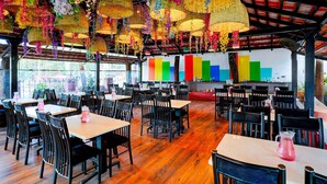 A restaurant with wooden flooring, black chairs, and tables. There are colorful hanging decorations and a colorful wall in the background. - Deluxe Olive Star (Mysore)
