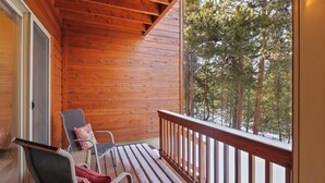Eine Holzterrasse mit zwei Stühlen und einer Bank, mit Blick auf einen verschneiten Wald.