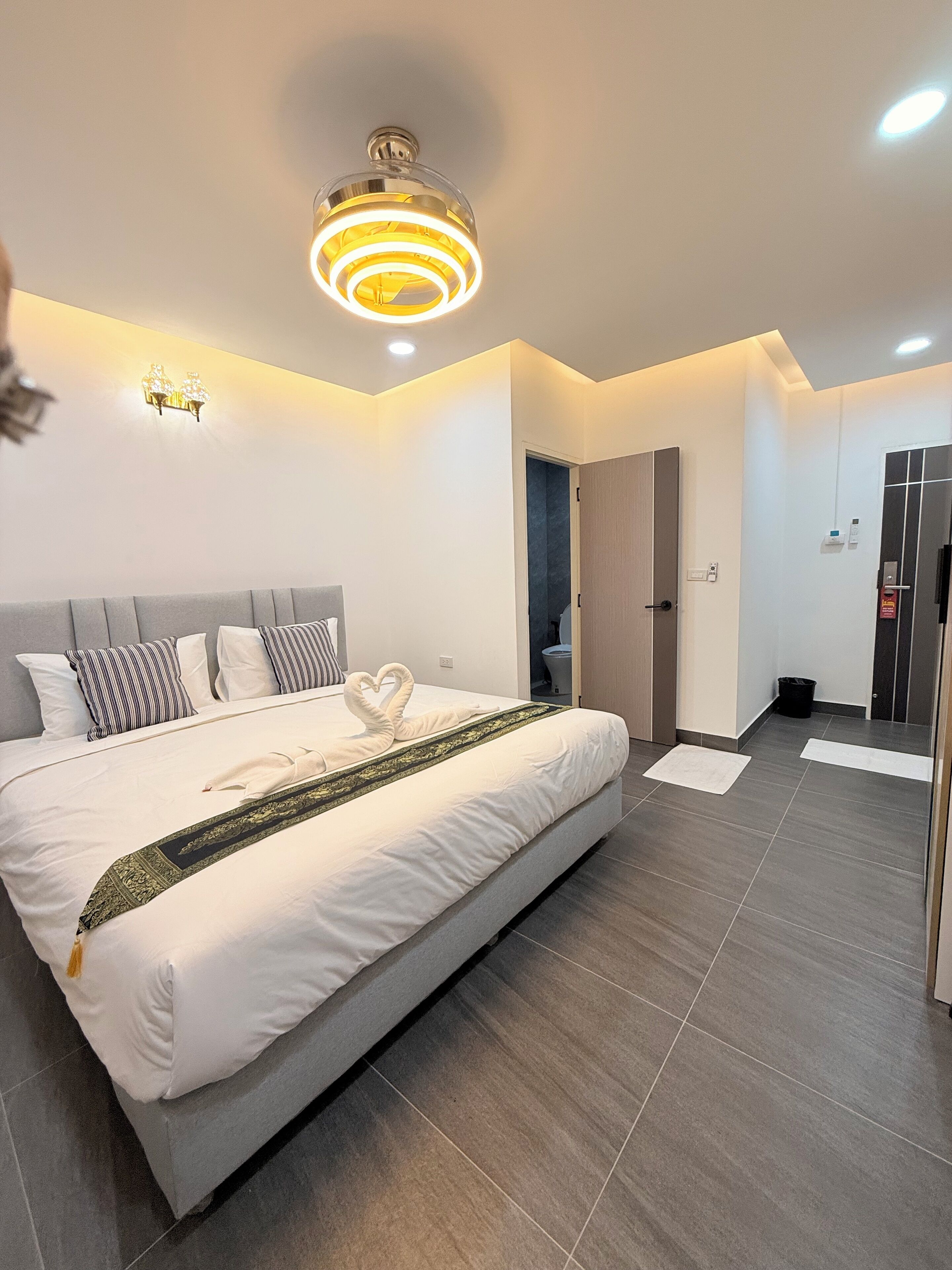 Una habitación de hotel moderna con una cama grande, un candelabro en el techo y una puerta que da al baño.