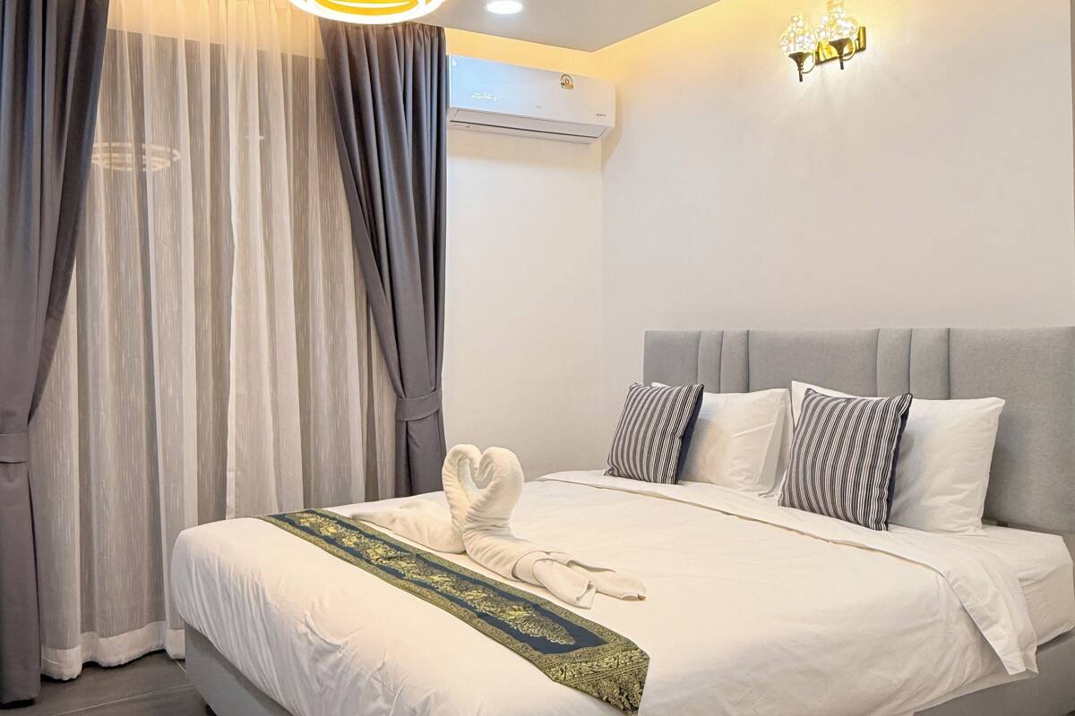 Een moderne hotelkamer met een groot bed, grijze gordijnen, een plafondlamp, een airconditioning en een wandlamp.