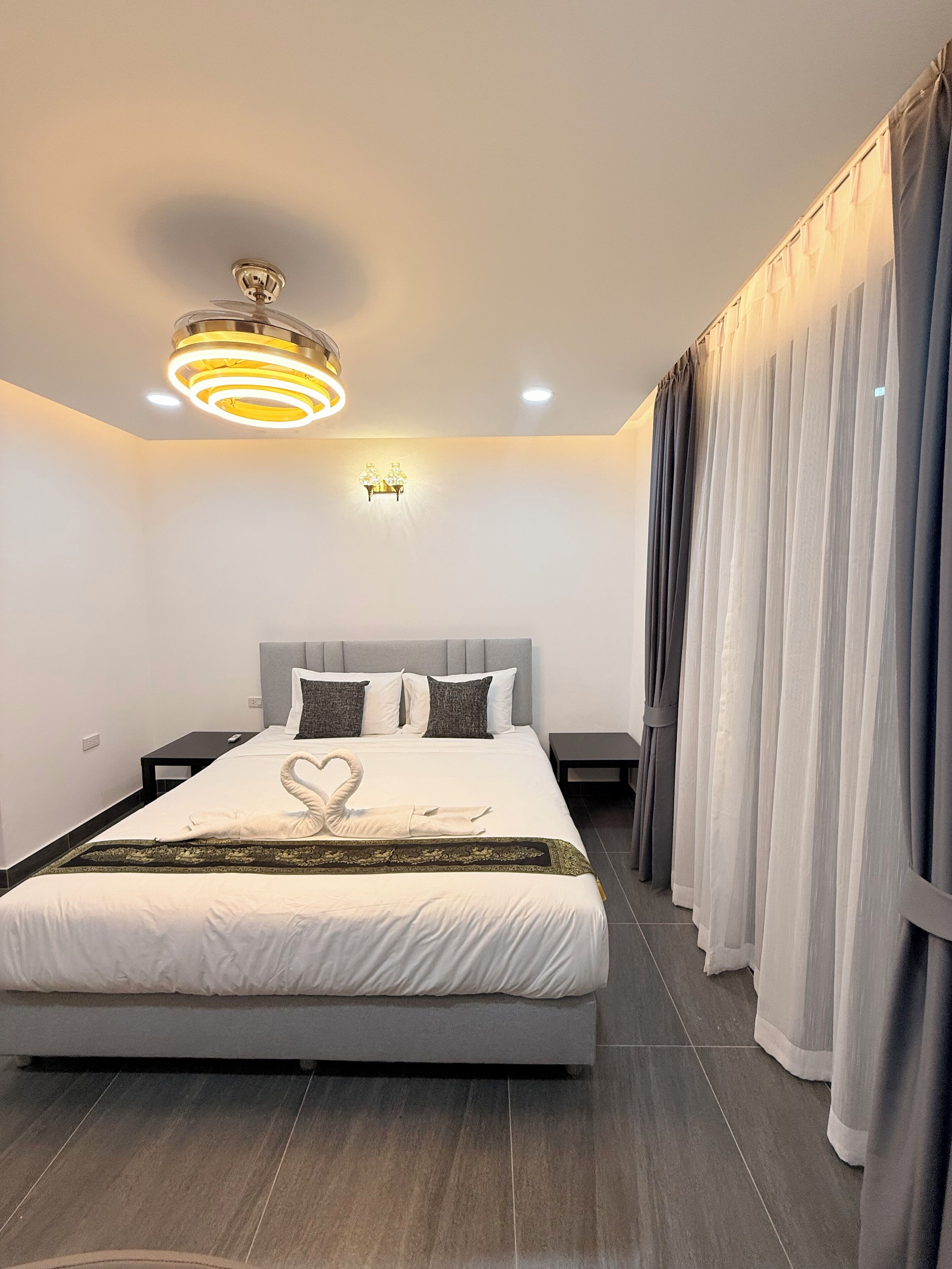 Une chambre d’hôtel moderne avec un grand lit, un lustre, une applique murale et un rideau.