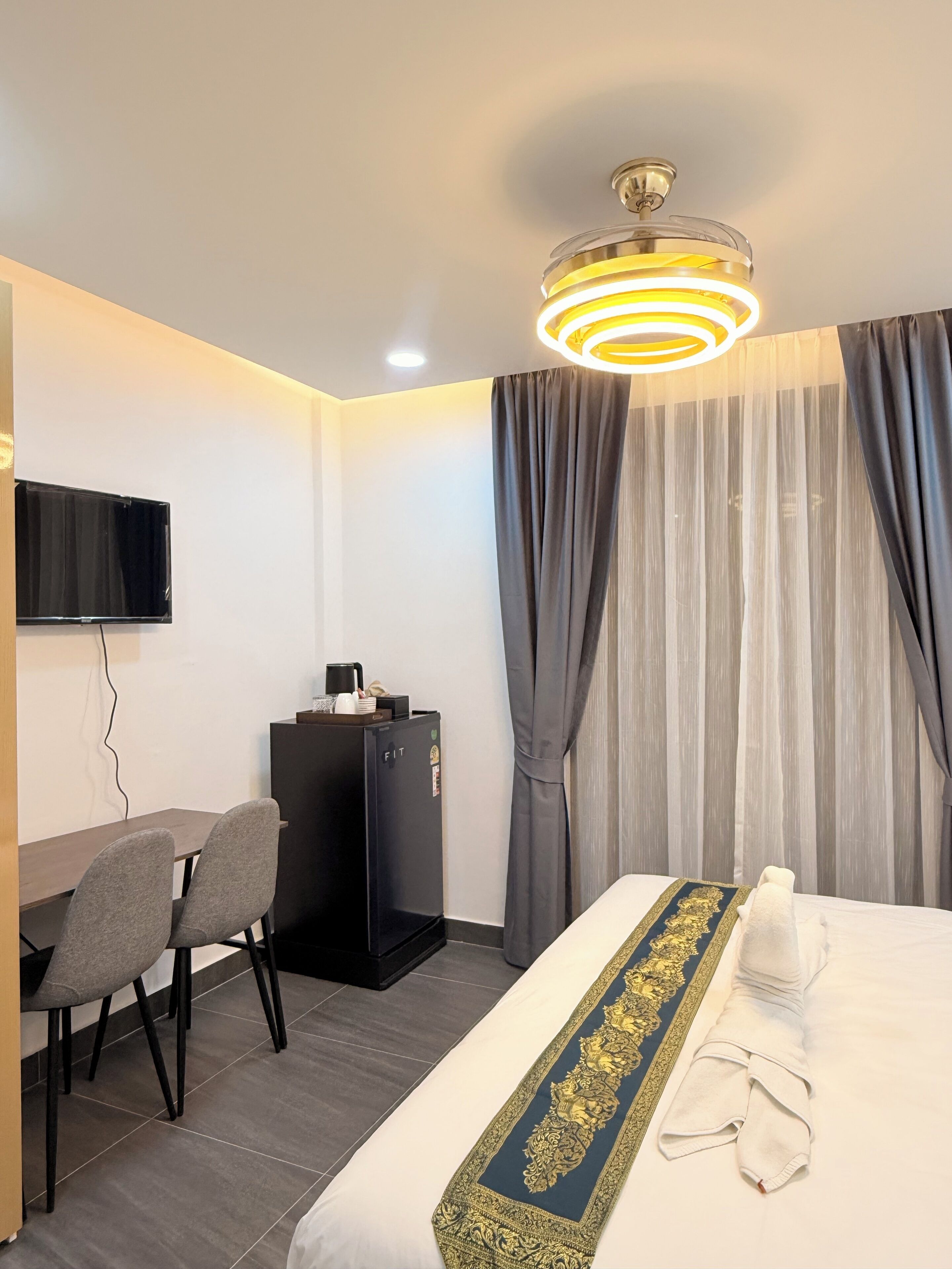 Ett hotellrum med en säng, ett skrivbord med en stol, en minibar och en tv på väggen.