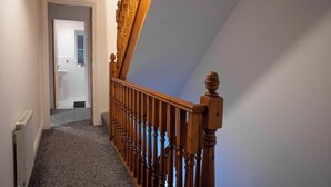 Een trap met houten spijlen die uitkomt op een plateau, bekleed met tapijt, en een witte radiator aan de muur.